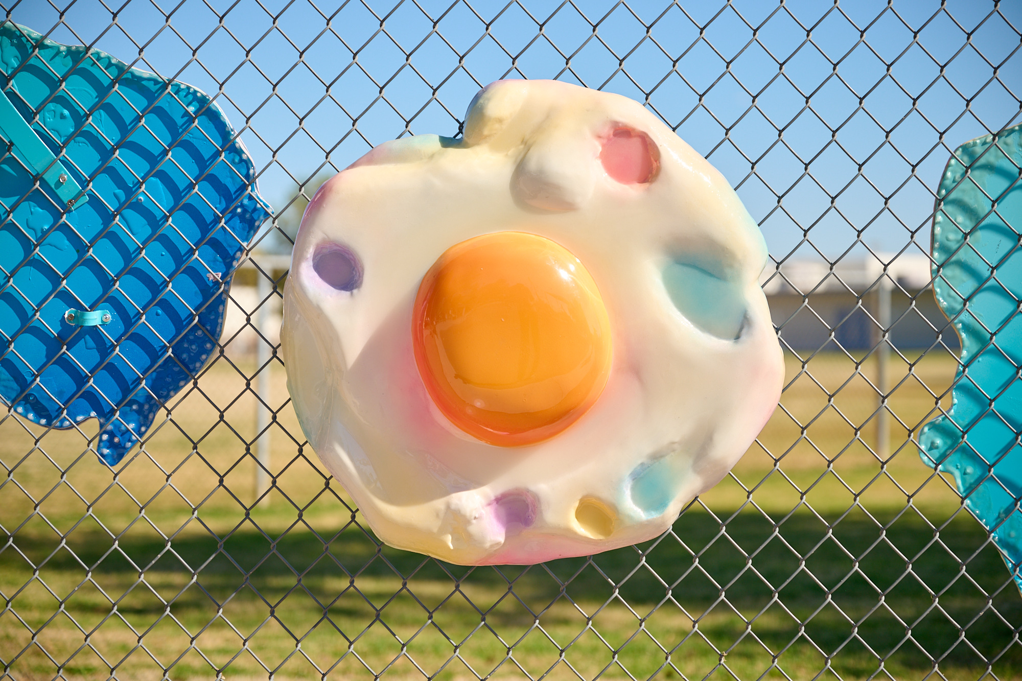 Close up image of a large, fried egg hanging on a fence. It is a sculpture.