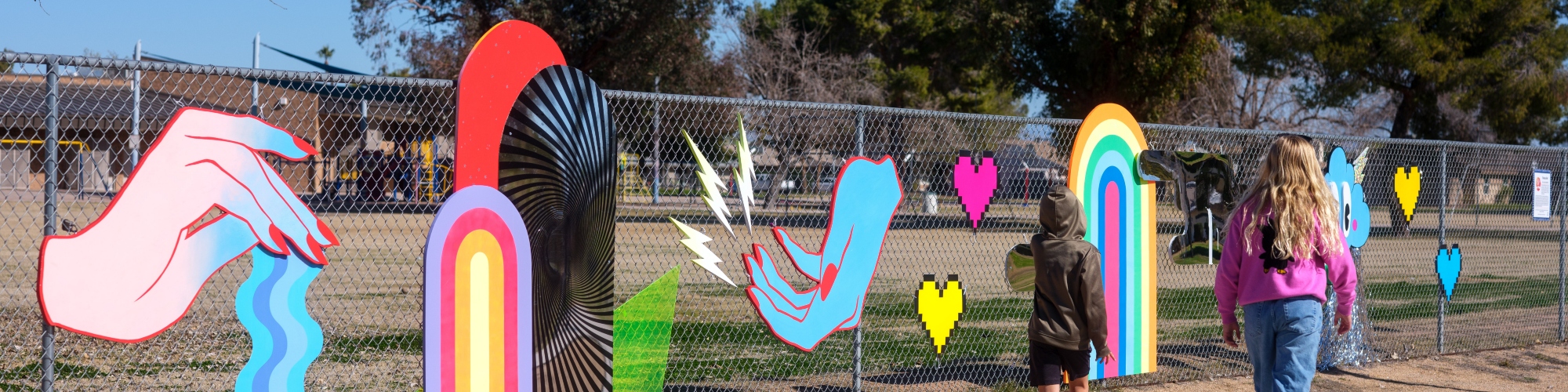 Photo of a colorful fence with graphic art and people walking passed.