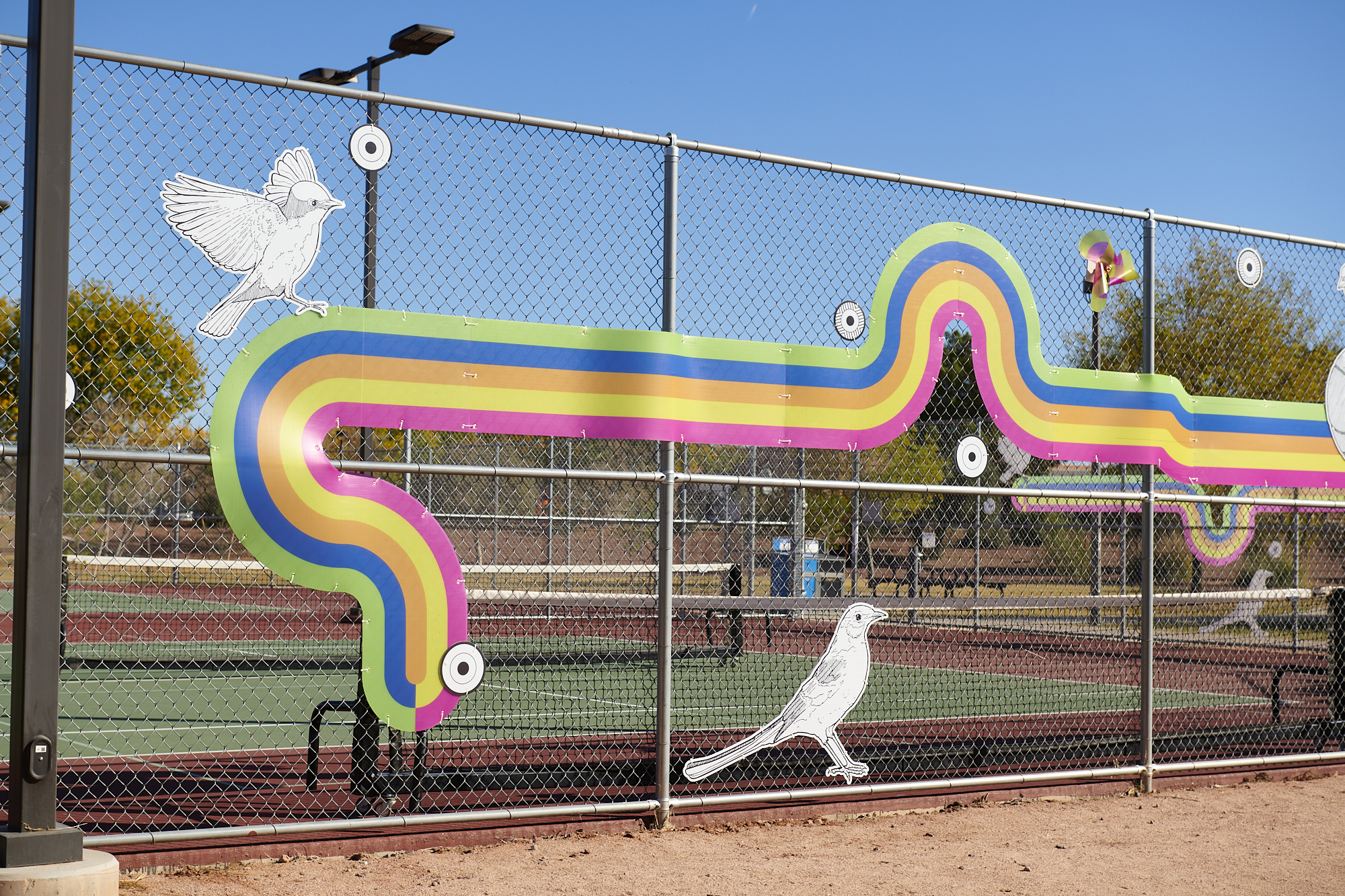 Closer image of a fence with colorful stripes and birds