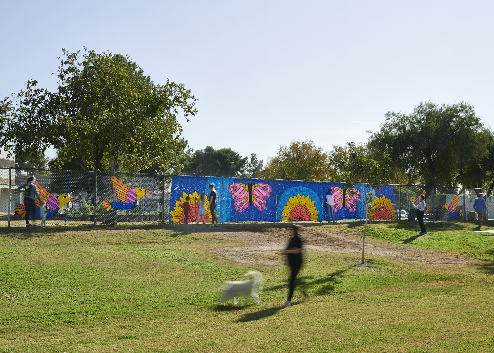 Landscape shot of a fence decorated with colorful sunflowers, butterflies, and birds.