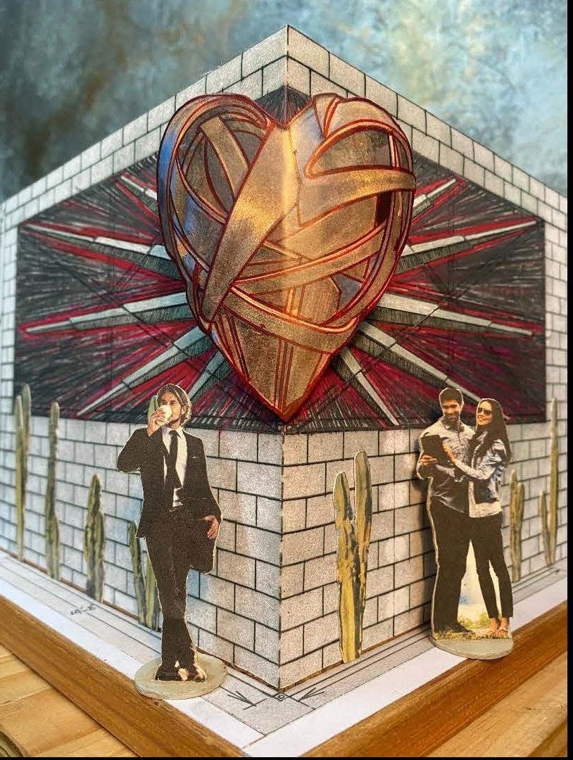 A physical paper mock-up of a heart sculpture on the corner of a building. The building is made of brick. There are three figures standing for scale. The heart sculpture begins at roughly head-height. It is a bronze color with red rays shining out from behind it.