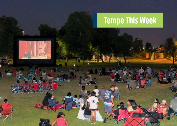 Groups of people sit on blankets and chairs in front of an inflatable movie screen showing Toy Story