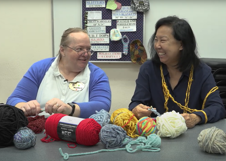 Tempe Needlewielders member Martha Kaupan sits next to Councilmember Arlene Chin at a table full of yarn.