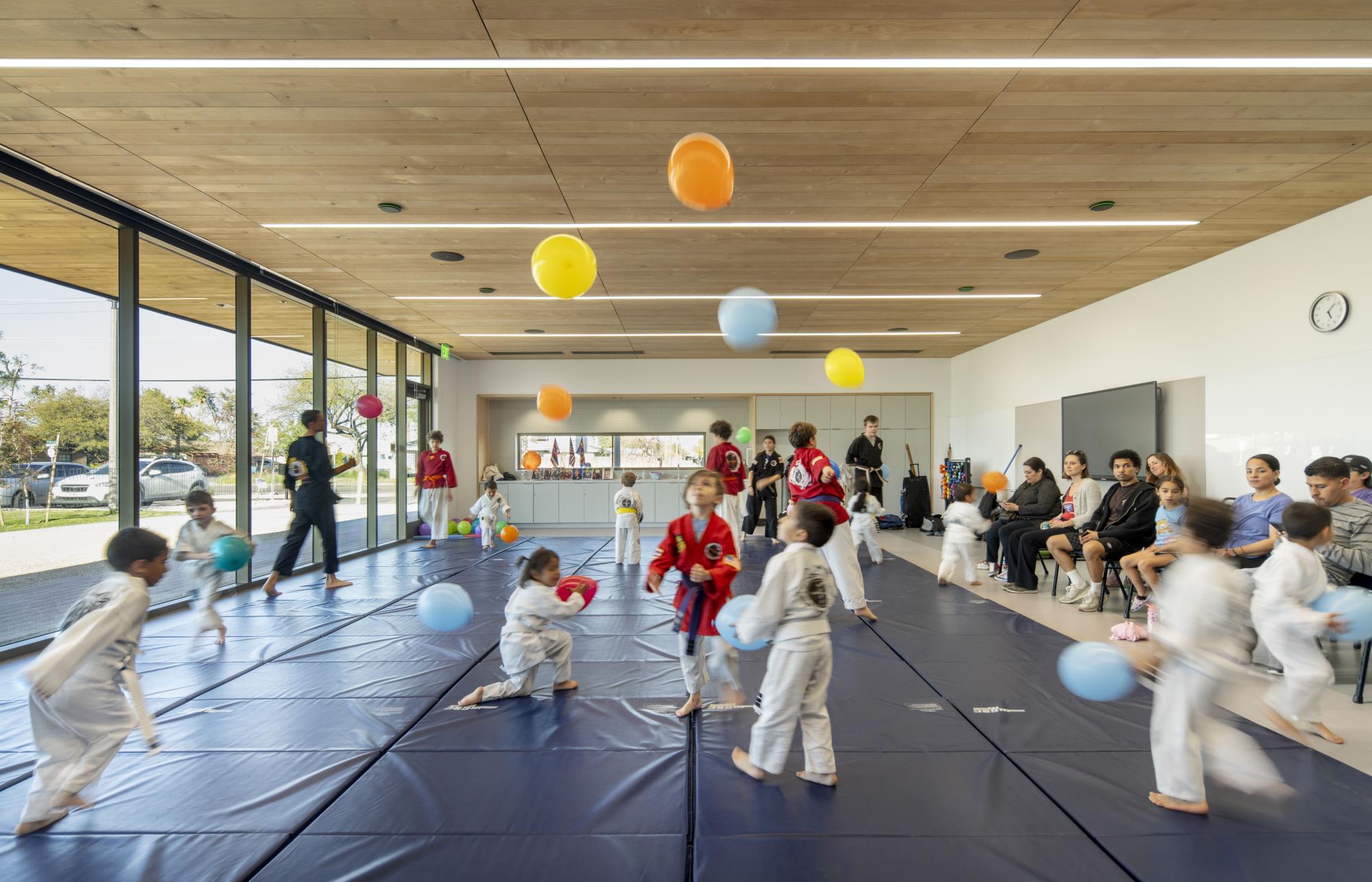 Image of a room with children running around in it. The room's floor is covered in foam pads and the children are wearing karate uniforms.