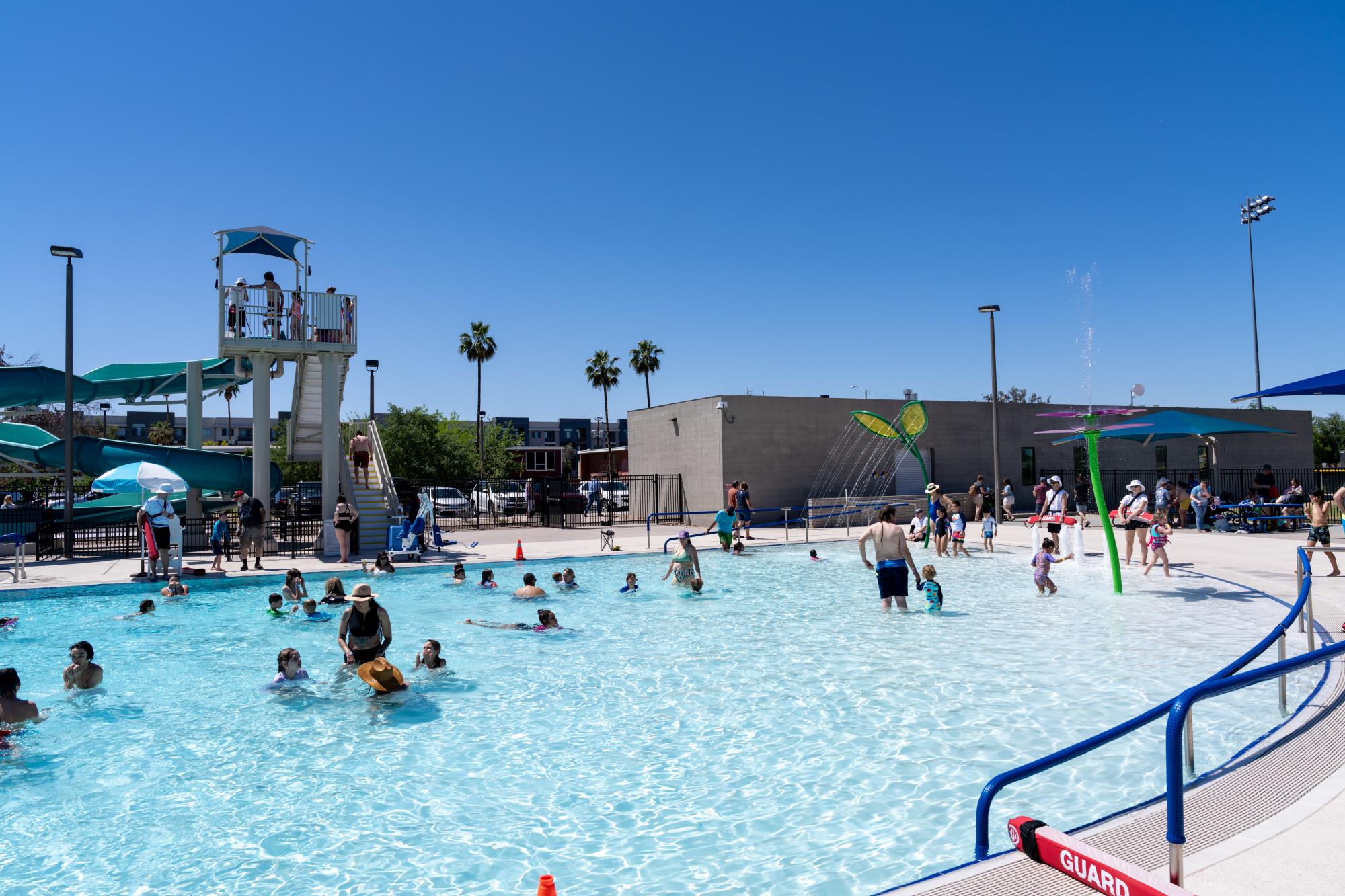 Image of a shallow swimming pool with people in it. In the background is a water slide.